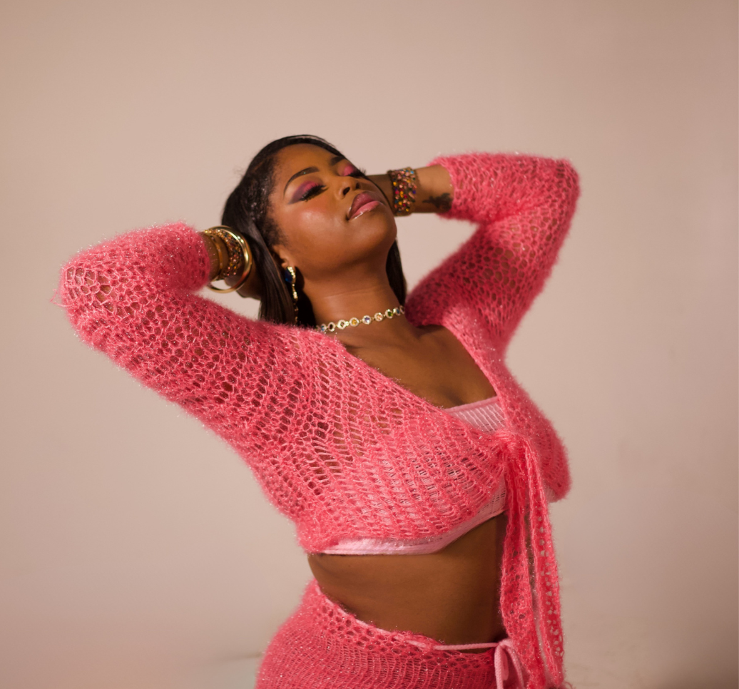 Woman wearing a pink crochet outfit posing against a plain background