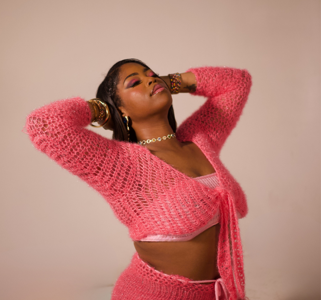 Woman wearing a pink crochet outfit posing against a plain background